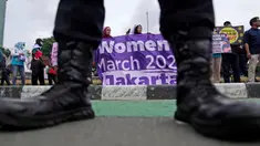 Seorang petugas polisi berjaga-jaga saat para aktivis membentangkan spanduk dalam unjuk rasa Hari Perempuan Internasional di Jakarta, Indonesia, Jumat, 8 Maret 2024. (AP Photo/Dita Alangkara)