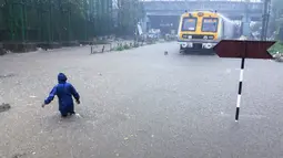 Seorang pria berjalan melintasi rel kereta api yang terendam banjir saat hujan lebat di Mumbai, India, Rabu (9/6/2021). Mumbai terendam banjir usai diguyur hujan lebat. (AP Photo/Rafiq Maqbool)