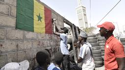 Pendukung menggantung bendera nasional Senegal di luar bengkel ban di Dakar (4/2/2022). Senegal akan bertanding melawan Mesir pada babak final Piala Afrika 2021 di Paul Biya stadium, Senin (7/2/2022) dini hari WIB besok. (AFP/Seyllou)