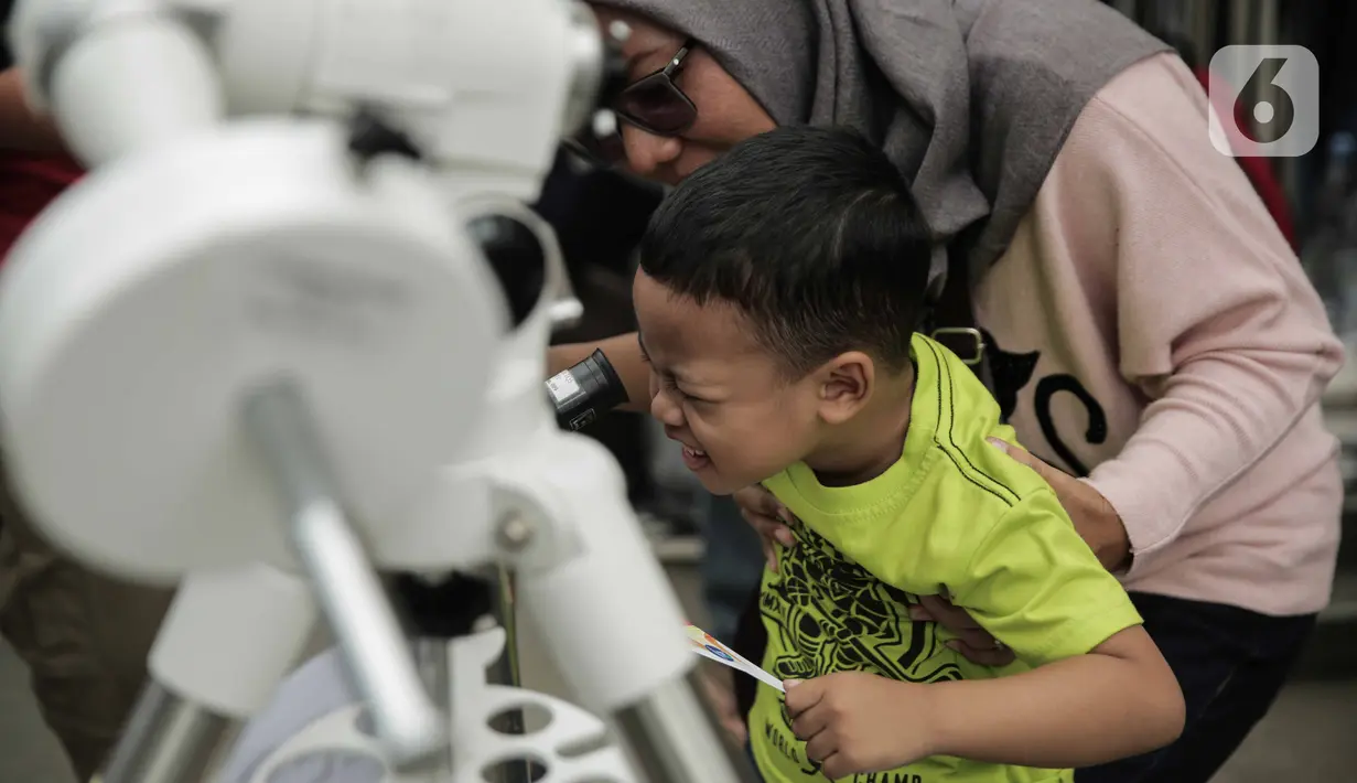 Pengunjung mengamati gerhana matahari cincin menggunakan teleskop di Planetarium Taman Ismail Marzuki, Jakarta, Kamis (26/12/2019). Planetarium menyediakan sekitar 10 teleskop dan kacamata khusus agar pengunjung bisa menyaksikan gerhana matahari cincin dengan aman. (Liputan6.com/Faizal Fanani)
