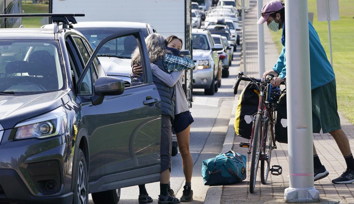 Seorang pengemudi mengucapkan selamat tinggal kepada kerabat yang dia turunkan dekat barisan kendaraan yang menunggu untuk memasuki Kanada di perbatasan Peace Arch, Blaine, Washington, Amerika Serikat, Senin (9/8/2021). (AP Photo/Elaine Thompson)