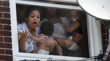 Wanita menggendong bayi menunggu bantuan setelah kebakaran terjadi di dalam gedung apartemen di Hazleton, Pennsylvania (26/7/2019). Pemadam kebakaran kota menggunakan truk menyelamatkan penghuni dari lantai tiga gedung. (Warren Ruda/Hazleton Standard-Speaker via AP)