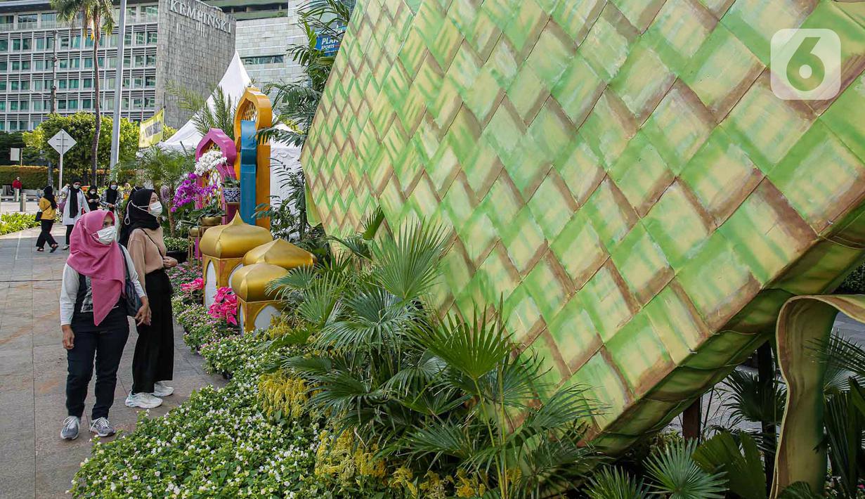 <p>Sejumlah warga memperhatikan dekorasi bertemakan Idul Fitri di kawasan Bundaran HI, Jakarta, Rabu (27/4/2022). Dekorasi berbentuk masjid, ketupat, dan bedug yang dihiasi oleh tanaman tersebut dalam rangka menyambut Idul Fitri 1443 Hijriah. (Liputan6.com/Faizal Fanani)</p>
