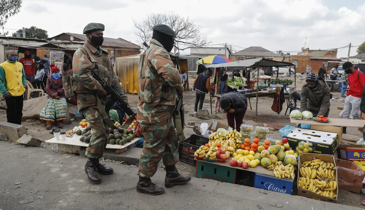 Orang-orang berdiri dan menonton di pasar makanan saat anggota Pasukan Pertahanan Afrika Selatan (SANDF) berpatroli di daerah mereka di Alexandra, Johannesburg, Kamis (15/7/2021). Patroli tersebut menyusul kerusuhan massa yang disebabkan dipenjaranya mantan Presiden Jacob Zuma. (Phill Magakoe/AFP)