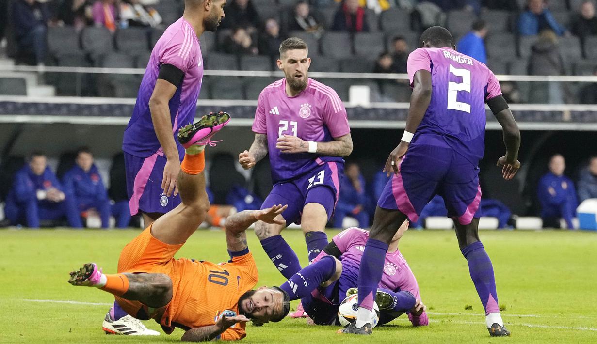 Pemain Belanda, Memphis Depay, terjatuh saat berebut bola dengan pemain Jerman pada laga persahabatan di Stadion Deutsche Bank Park, Frankfurt, Rabu (27/3/2024). Jerman menang dengan skor 2-1. (AP Photo/Martin Meissner)