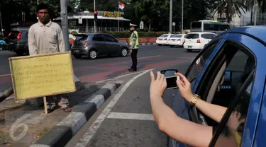 Penumpang taksi mengabadikan aksi Syaripudin Dodo (59) di Bundaran HI, Jakarta, Kamis (30/7/2015). Kakek ini meminta pertolongan pengguna jalan untuk membiayai sekolah cucunya di Perguruan Islam Al Masthuriyah Sukabumi. (Liputan6.com/Johan Tallo)