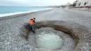 Seorang pria turun melihat kawah misterius berisi air payau yang muncul di Pantai Lido, Nice, Prancis, Kamis (1/2). Lubang selebar 5 meter dan sedalam 2 meter itu membuat banyak warga sekitar kebingungan. (VALERY HACHE/AFP)