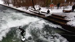Seorang pria menaklukkan ombak saat berselancar di Sungai Eisbach selama hari musim dingin di Munich, Jerman, 4 Januari 2017. Sungai ini dipakai sebagai tempat berselancar sejak 1972 namun baru secara resmi diperbolehkan pada 2010. (Mark RALSTON/AFP)