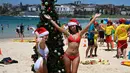 Turis memakai topi Santa foto di sebelah pohon Natal selama Hari Natal di Pantai Bondi di Sydney, Australia (25/12). (AFP Photo/Peter Parks)
