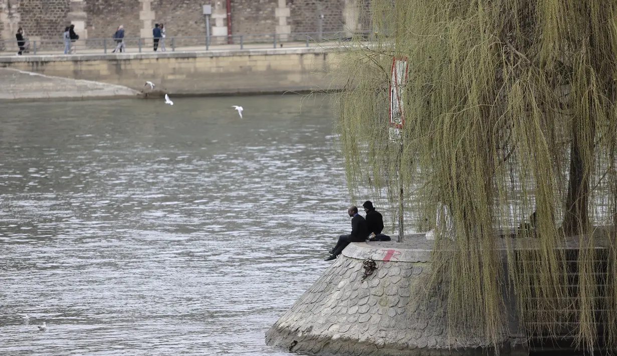 Orang-orang duduk di tepi sungai Seine di Paris, Rabu (3/3/2021).  Tingkat infeksi COVID-19 tetap tinggi selama beberapa minggu, dan pasien virus menempati 70% unit perawatan intensif negara itu. (AP Photo/Lewis Joly)