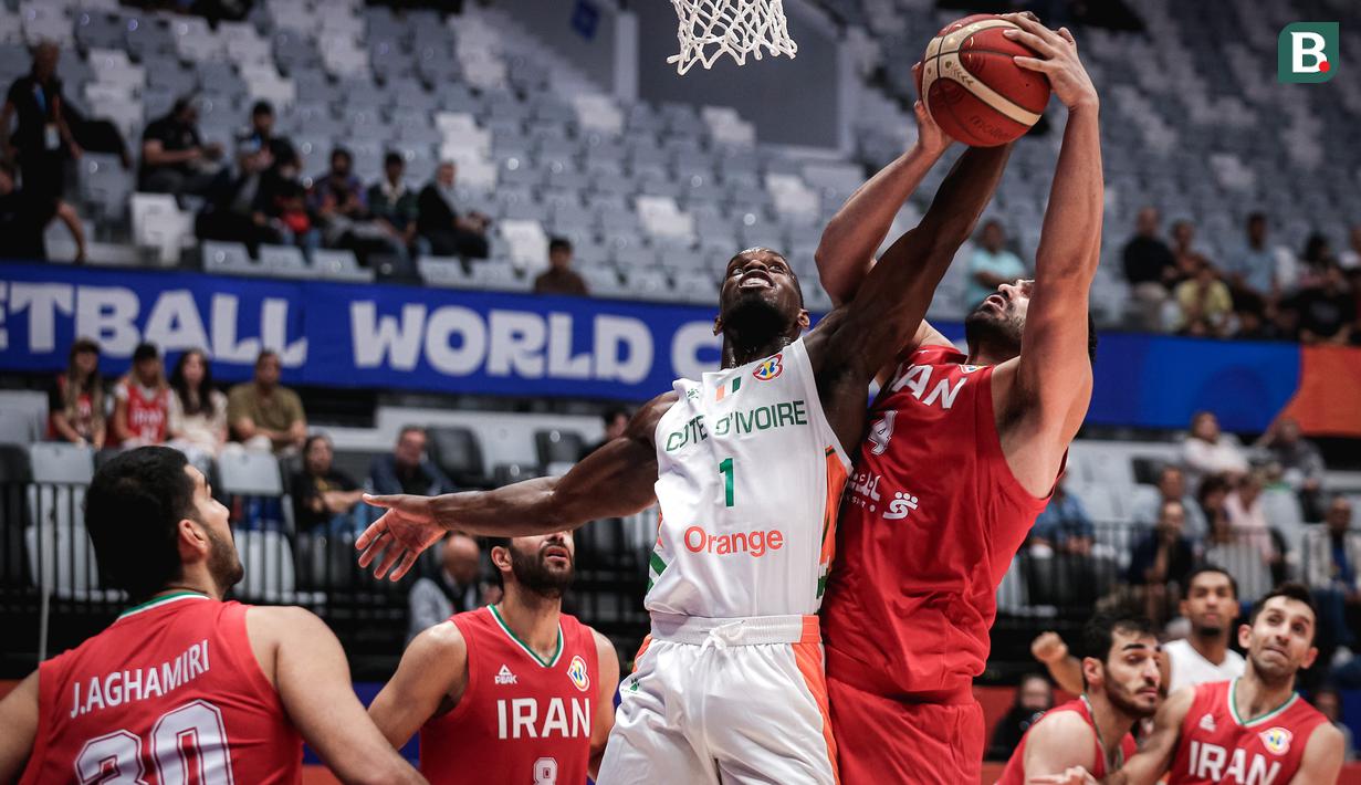 <p>Pebasket Pantai Gading, Charles Abouo (tengah) berusaha mencetak poin dihalangi pebasket Iran, Meisam Merzaei pada laga kedua Grup G Piala Dunia FIBA 2023 di Indonesia Arena, Senayan, Jakarta, Senin (28/08/2023). (Bola.com/Bagaskara Lazuardi)</p>
