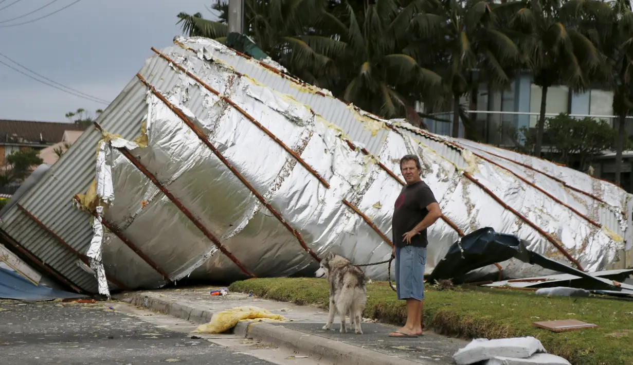 Warga berjalan bersama anjingnya melewati atap rumah yang terbawa badai tornado di Kurnell pinggir Sydney, Rabu (16/12). Badai dengan hujan es disertai angin berkekuatan sampai 200 km per jam melanda kawasan tersebut. (REUTERS/Jason Reed)