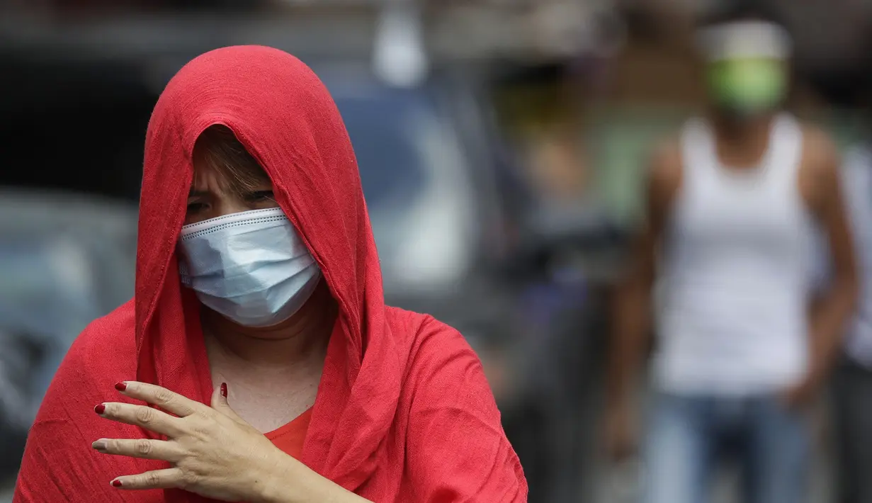 Seorang wanita mengenakan masker berjalan di luar desa yang dikunci di Manila, Filipina (11/3/2021). Kota-kota lain di ibu kota memberlakukan kembali penguncian di beberapa lingkungan dan jam malam yang lebih panjang setelah mendeteksi infeksi baru. (AP Photo/Aaron Favila)