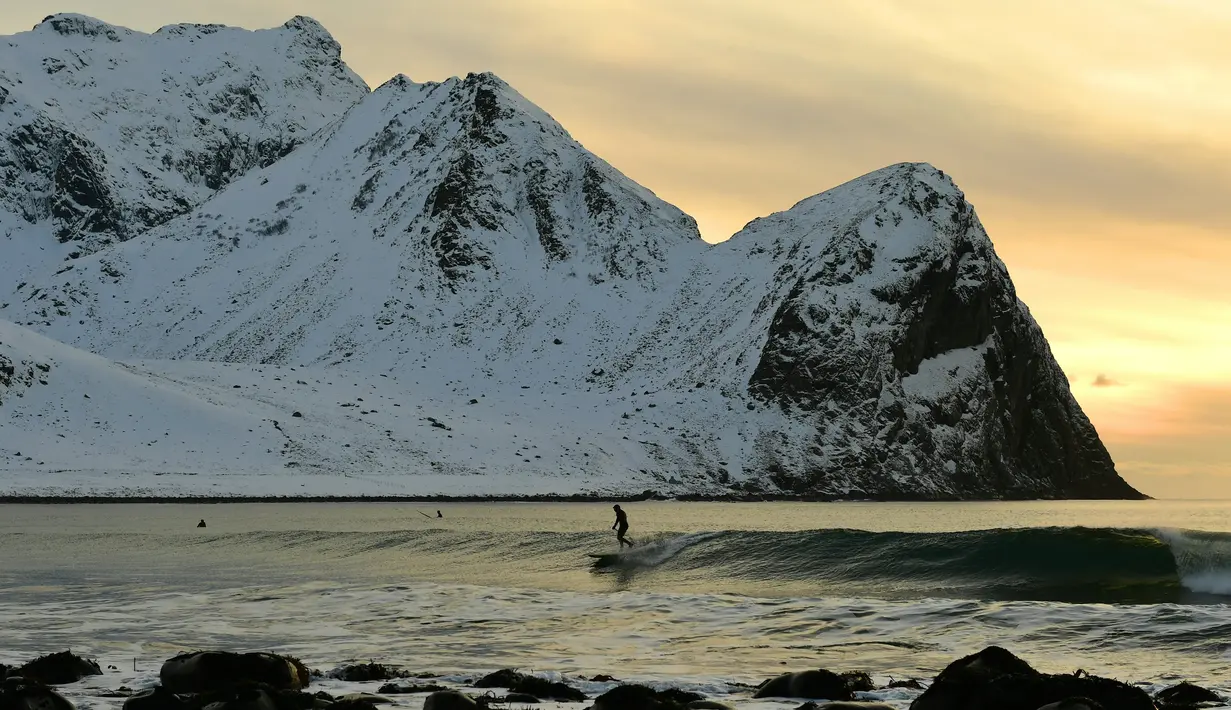 Peselancar menikmati gelombang ombak saat berselancar di pantai bersalju Flackstad di Kepulauan Lofoten, Lingkar Arktik, pada 12 Maret 2016. Suhu laut mencapai 5 derajat celcius dan suhu udara hingga 0 derajat celcius. (AFP/Olivier Morin)