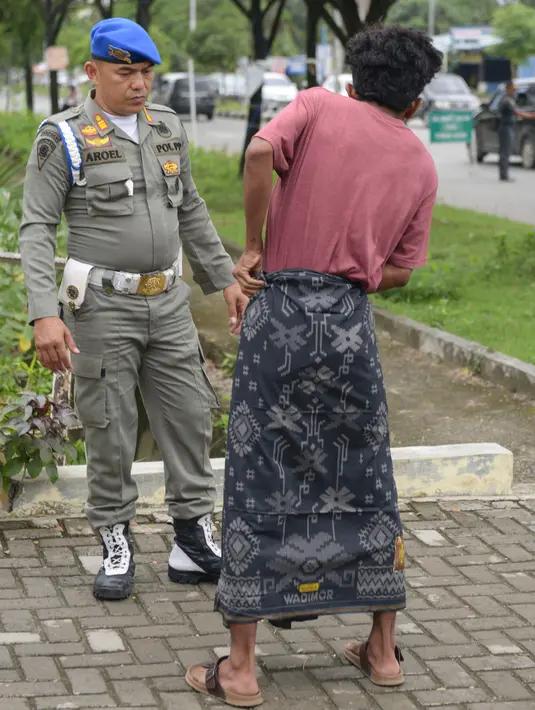 Seorang pengendara bercelana pendek mengenakan kain sarung yang diberikan polisi Syariat Islam saat razia penertiban hukum syariat islam di Banda Aceh, Aceh, Selasa (19/9). Razia itu digelar oleh Satpol PP dan Wilayatul Hisbah. (CHAIDEER MAHYUDDIN/AFP)