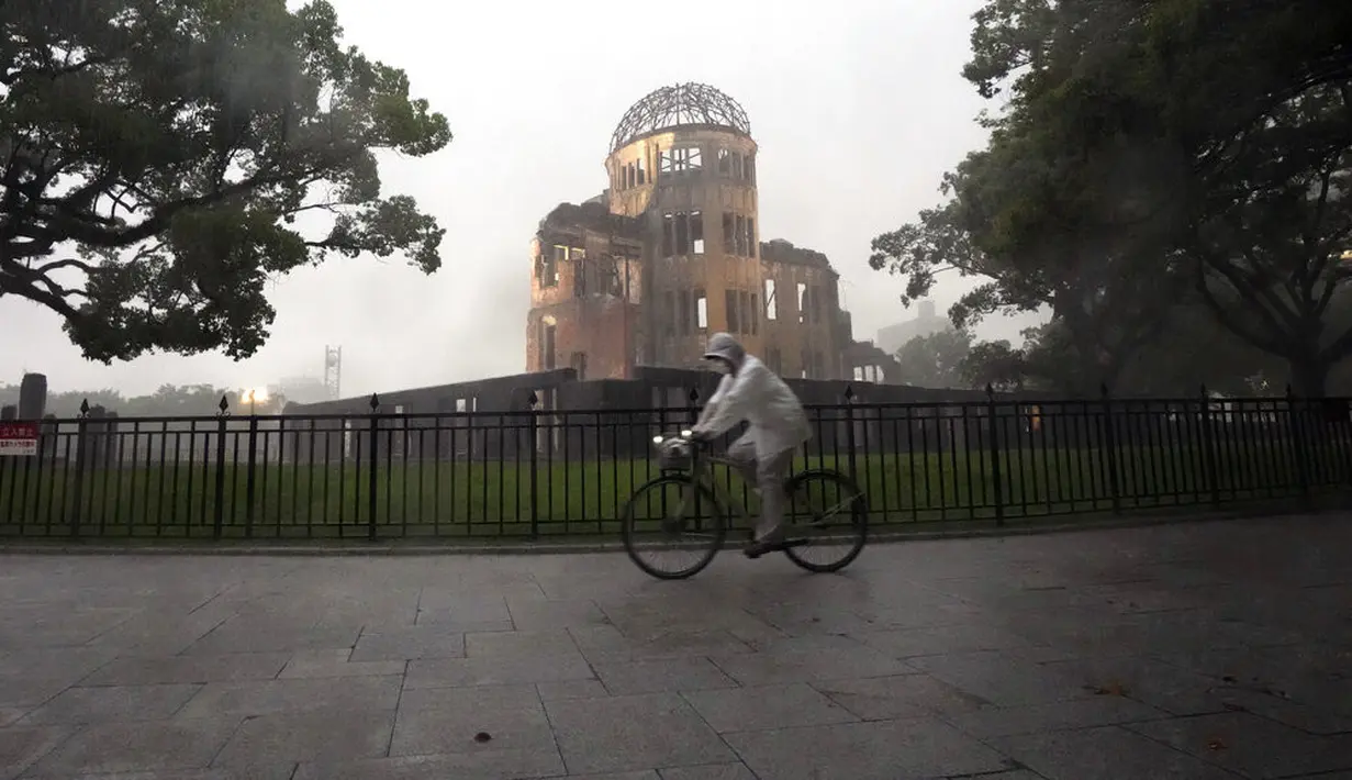 Seorang pengendara sepeda terjebak dalam hujan lebat di dekat Kubah Bom Atom di Hiroshima, Jepang barat, Kamis (15/7/2021). Atomic Bomb Dome atau kubah bom atom yang merupakan bagian dari taman perdamaian Hiroshima. AP Photo/Eugene Hoshiko)