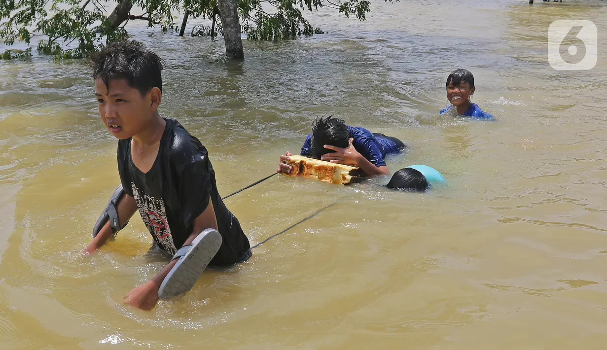 Anak-anak melintasi banjir di Desa Sukalaksana Kabupaten Bekasi, Jawa Barat, Senin (22/02/2021). Ketinggian air di sekitar permukiman warga mencapai 1,5 meter. (Liputan6.com/Herman Zakharia)
