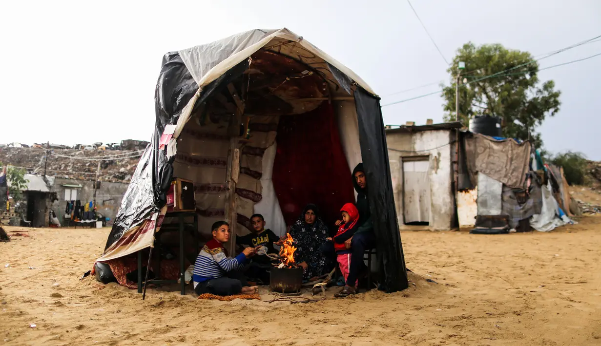Warga Palestina menghangatkan diri di sekitar api tungku di area permukiman kumuh sebuah kamp pengungsi saat cuaca badai di Kota Khan Younis, Jalur Gaza selatan, pada 26 November 2020. (Xinhua/Yasser Qudih)