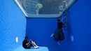 Pengunjung berfoto di karya seni Swimming Pool dalam sebuah pameran di Museum CAFA, Beijing, 23 Juli 2019. Bagian atas karya seni unik itu berlapis kaca transparan yang dilapisi air sedalam 10 cm, sedangkan bagian bawahnya merupakan ruang kosong dengan dinding berwarna biru muda. (WANG Zhao/AFP)