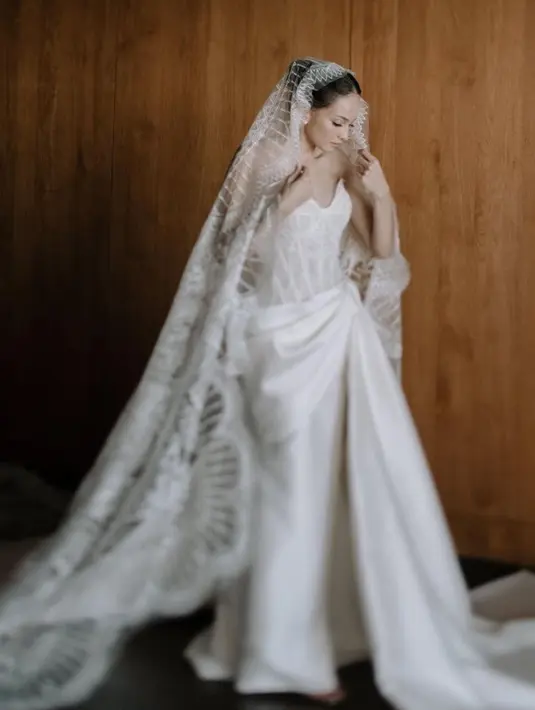 Enzy Storia juga tampil dengan gaun pernikahan warna putih model bustier lengkap bawahan satin dan veil berbordir dari Monica Ivena. [@enzystoria]