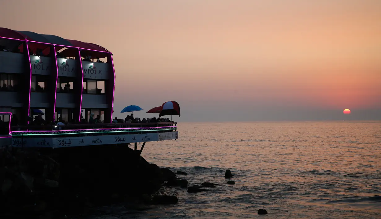 Matahari terbenam ketika keluarga berkumpul di sebuah restoran di sepanjang pantai di Kota Gaza (10/6/2019). Pergi ke restoran di dekat pantai merupakan opsi bagi warga Palestina untuk menikmati suasana alam. (AFP Photo/Mohammed Abed)