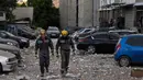 Tim penyelamat berjalan melewati mobil-mobil yang rusak di luar sebuah bangunan tempat tinggal bertingkat, yang sebagian hancur setelah serangan pesawat tak berawak pada malam hari di Kyiv pada 30 Mei 2023. (Sergei SUPINSKY/AFP)
