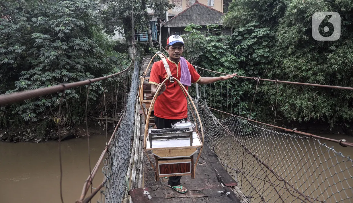 Pedagang melintasi jembatan gantung yang sudah tidak layak di kawasan Srengseng Sawah, Jakarta, Sabtu (12/6/2021). Kondisi jembatan gantung yang menjadi akses warga dari Cimanggis menuju Srengseng Sawah atau sebaliknya tersebut beralaskan bambu serta seng. (merdeka.com/Iqbal S. Nugroho)