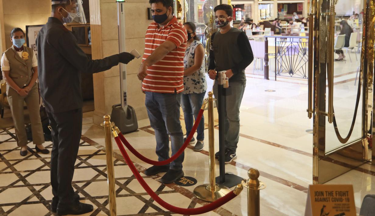 Seorang karyawan memeriksa suhu pejuang COVID-19 dan keluarganya yang tiba saat bioskop dibuka kembali dengan pemutaran khusus untuk mereka di bioskop PVR di New Delhi, India (15/101/2020). Bioskop telah menerapkan protokol kesehatan yang ketat. (AP Photo/Manish Swarup)
