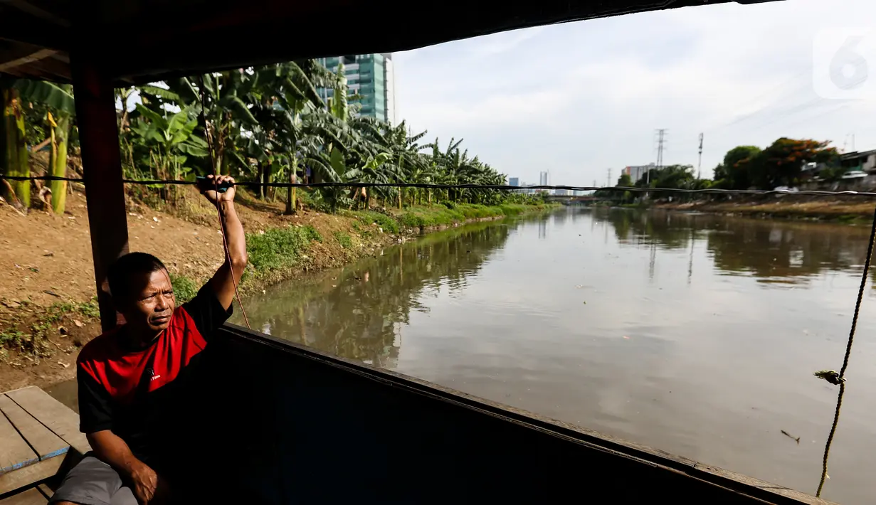 Romli, pemilik perahu eretan duduk menunggu warga menyeberangi Banjir Kanal Barat, Jatipulo, Jakarta, Senin (31/01/2022). Keberadaan perahu eretan sepi penumpang sejak dibangunnya jembatan penyeberangan dan ramainya moda transportasi. (Liputan6.com/Fery Pradolo)