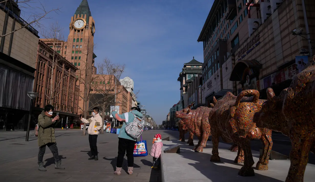 Warga yang mengenakan masker berfoto bersama seorang anak dekat patung banteng berjudul "Five Bulls Gathering Fortune" di distrik perbelanjaan Wangfujing, Beijing, China, Rabu (14/12/2022). Mulai hari ini, Komisi Kesehatan Nasional China melaporkan penurunan kasus harian COVID-19 sejak pemerintah melonggarkan pengujian PCR setelah kasus harian mencapai rekor tertinggi. (AP Photo/Andy Wong)