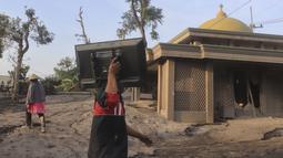 Seorang pria membawa televisi saat berjalan melewati masjid yang sebagian terkubur abu vulkanik dari letusan Gunung Semeru di desa Kajar Kuning di Lumajang, Jawa Timur, Indonesia, Senin, 5 Desember 2022. Gunung Semeru mengalami kenaikan dari Level III (Siaga) menjadi Level IV (Awas) sejak 4 Desember 2022 pada pukul 12.00 WIB, sehingga Pusat Vulkanolologi dan Mitigasi Bencana Geologi memberikan beberapa rekomendasi agar masyarakat mematuhinya. (AP Photo/Imanuel Yoga)