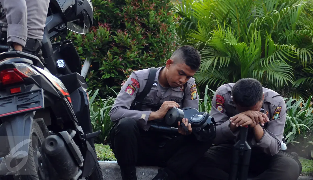 Polisi duduk beristirahat saat berjaga di depan Istana Negara, Jakarta, Jumat (4/11). Ribuan aparat gabungan disiagakan saat massa melakukan aksi menuntut penegakan hukum kasus dugaan penistaan agama. (Liputan6.com/Helmi Fithriansyah)