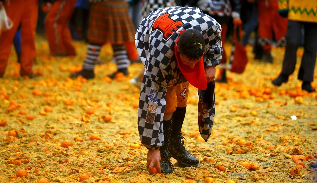 Seorang peserta mengumpulkan jeruk di tanah saat perang-perangan selama karnaval di kota Ivrea, Italia, Minggu (7/2). Peserta yang dibagi menjadi dua tim ini saling melempar jeruk menggunakan kostum dan aksesoris lengkap. (REUTERS/Stefano Rellandini)