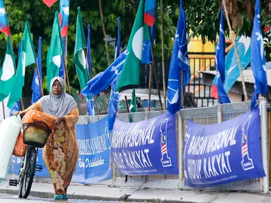 Seorang wanita mendorong sepedanya di samping bendera-bendera partai politik, Kuala Lumpur, Malaysia, Senin (7/5). Malaysia akan melangsungkan pemilu pada 9 Mei 2018. (AP Photo/Aaron Favila)