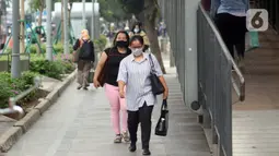 Warga mengenakan masker melintas di trotoar Jalan Jenderal Sudirman, Jakarta, Kamis (9/7/2020). Berdasar data yang diumumkan pemerintah pada Kamis (9/7) ada penambahan 2.657 orang yang terinfeksi COVID-19 sehingga jumlah penderita menjadi 70.736. (Liputan6.com/Helmi Fithriansyah)