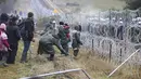 Migran dari Timur Tengah dan tempat lain mendobrak pagar saat mereka berkumpul di perbatasan Belarusia-Polandia dekat Grodno, Belarus, Senin (8/11/2021). (Leonid Shcheglov/BelTA via AP)