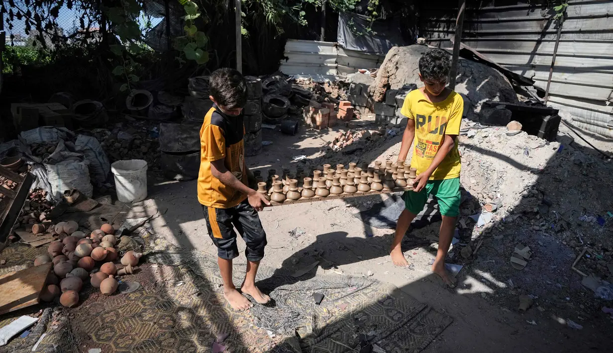 Anak-anak membawa bejana tanah liat di salah satu bengkel tembikar tertua di Beit Lahia, Jalur Gaza, 15 Agustus 2022. (AP Photo/Hatem Moussa)