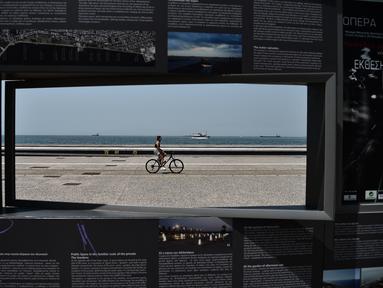Seorang wanita mengendarai sepeda di sepanjang tepi pantai Thessaloniki, Yunani utara (23/6/2021).  Yunani bersiap menghadapi gelombang panas pertama musim panas, mendorong suhu siang hari ke wilayah 40+ Celcius di banyak bagian negara. (AFP/Sakis Mitrolidis)