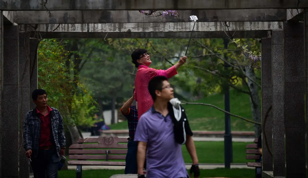 Seorang wanita menggunakan ponselnya berselfie di sebuah taman di Beijing (19/4). Beijing adalah ibu kota Republik Rakyat Tiongkok dan merupakan salah satu kota terpadat di dunia. (AFP Photo/Wang Zhao)