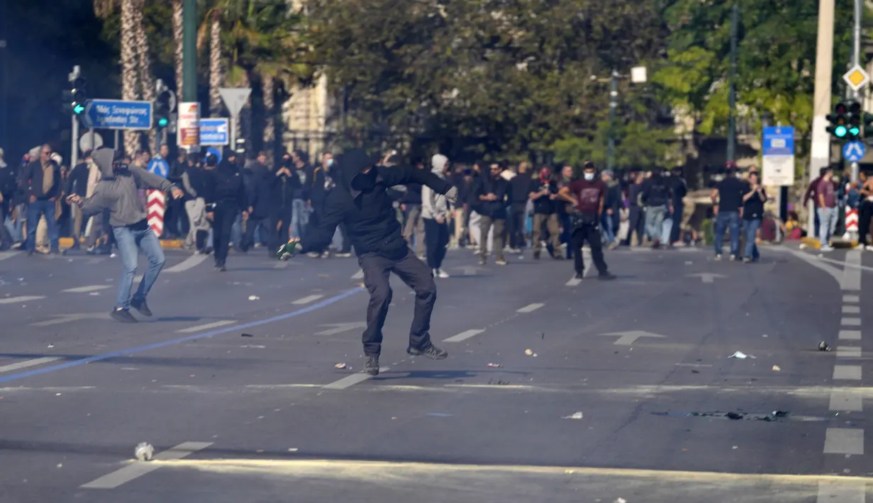 Seorang pengunjuk rasa berkerudung bersiap untuk melemparkan bom molotov ke polisi anti huru hara di luar Parlemen Yunani selama bentrokan di Athena, Yunani, Rabu (9/11/2022). Ribuan pengunjuk rasa berbaris melalui jalan-jalan Athena dan kota Thessaloniki di Yunani utara sebagai pekerja publik dan beberapa sektor swasta meninggalkan pekerjaan untuk pemogokan umum 24 jam terhadap kenaikan harga.  (AP Photo/Petros Giannakouris)