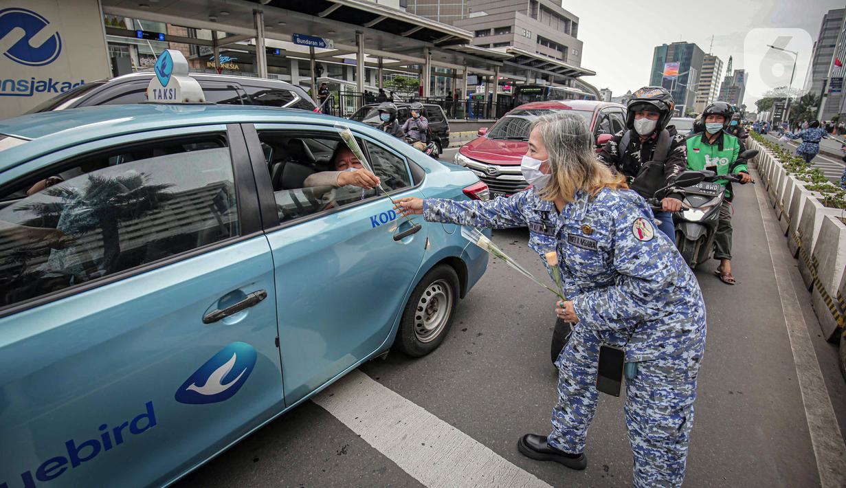 Perserta yang tergabung dalam Forum Kader Bela Negara DKI Jakarta membagikan bunga dan masker kepada pengguna jalan di Jalan Thamrin, Jakarta, Rabu (22/12/2021). Aksi tersebut merupakan bentuk apresiasi terhadap kaum perempuan terutama pada peringatan Hari Ibu. (Liputan6.com/Faizal Fanani)