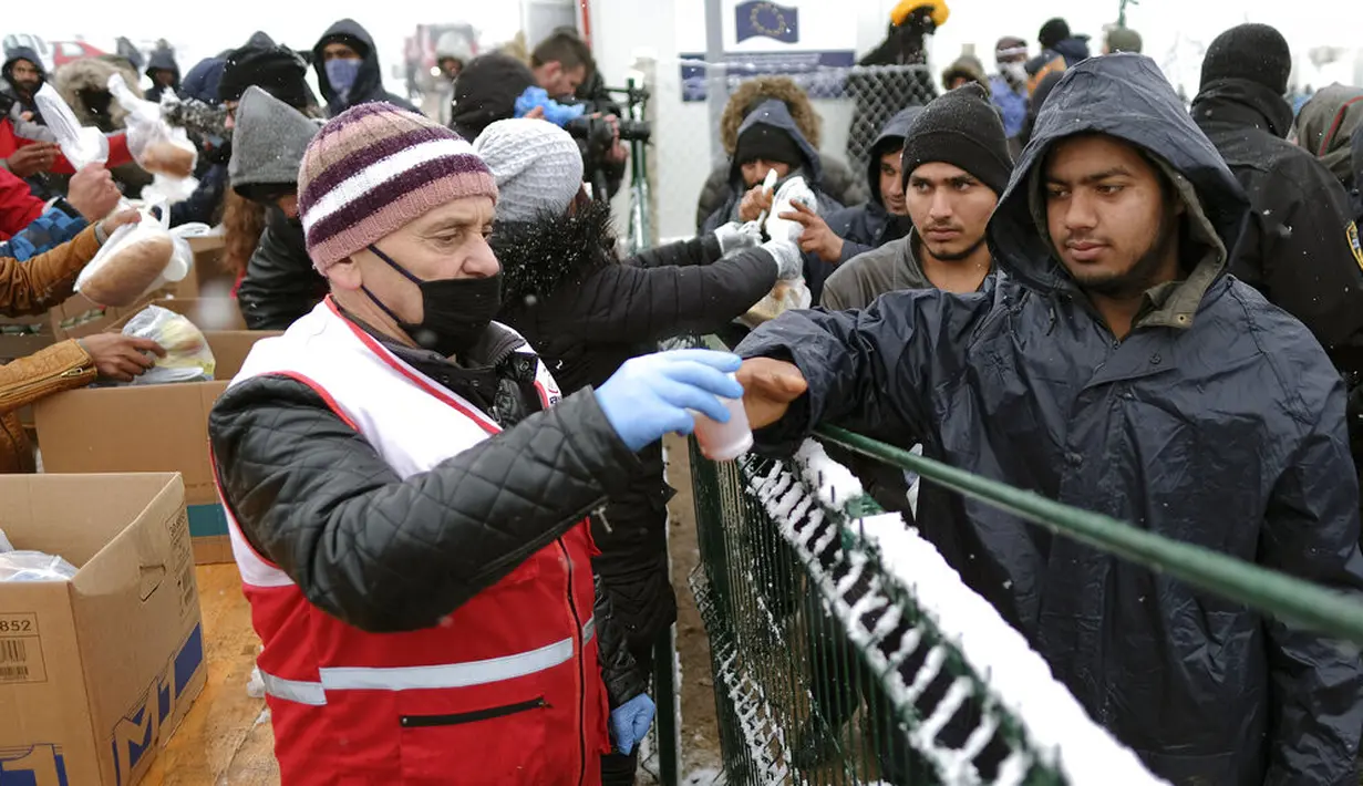 Para imigran menerima bantuan makanan saat hujan salju di Kamp Lipa, luar Bihac, Bosnia, Jumat (8/1/2021). Cuaca bersalju dan musim dingin telah membawa lebih banyak penderitaan bagi ratusan imigran yang terjebak selama berhari-hari di kamp tersebut. (AP Photo/Kemal Softic)
