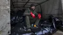 Seorang pekerja kamar jenazah duduk di atas kantong jenazah sebelum diangkut untuk dimakamkan di kuburan massal di pinggiran Mariupol, Ukraina, 9 Maret 2022. (AP Photo/Evgeniy Maloletka)