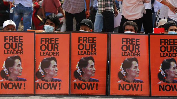 Pengunjuk rasa antikudeta duduk di belakang poster dengan gambar pemimpin Myanmar yang digulingkan Aung San Suu Kyi selama unjuk rasa di Yangon, Myanmar, Senin (22/2/2021). Meski ada peringatan dari militer Myanmar, peserta demonstrasi tidak gentar. (AP Photo)