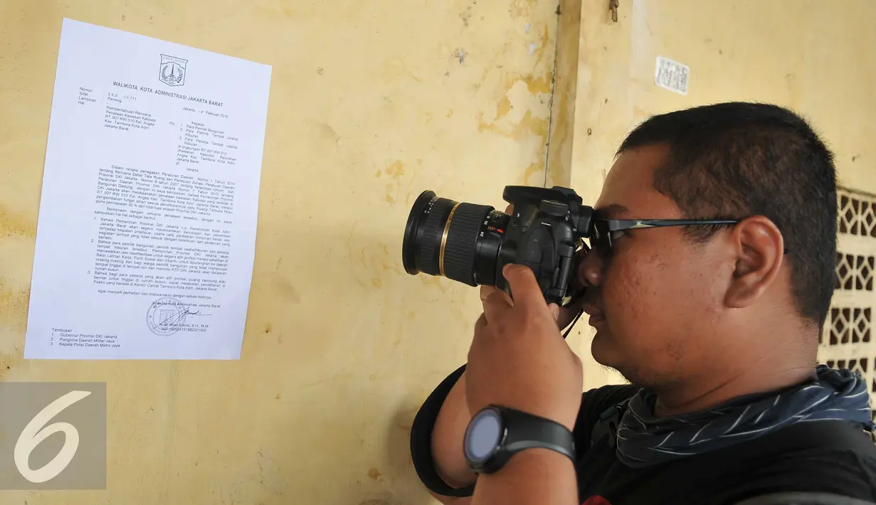 Fotografer memotret surat pemberitahuan dari Pemprov DKI Jakarta yang tertempel di kawasan Kalijodo, Jakarta, Selasa (16/2). Surat edaran tersebut berisi antara lain akan adanya pengembalian fungsi kawasan Kalijodo. (Liputan6.com/Gempur M Surya)