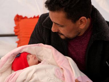 Khalil al-Suwadi menggendong keponakannya Afraa, bayi Suriah yang lahir di bawah reruntuhan setelah gempa bumi 6 Februari yang melanda Turki dan Suriah yang menewaskan orang tua dan saudara kandungnya, di kota Jindayris yang dikuasai pemberontak di Suriah utara, Selasa (21/2/2023). Kini, bayi yang diberi nama Afraa al-Suwadi tersebut diasuh oleh pamannya. (Rami al SAYED / AFP)