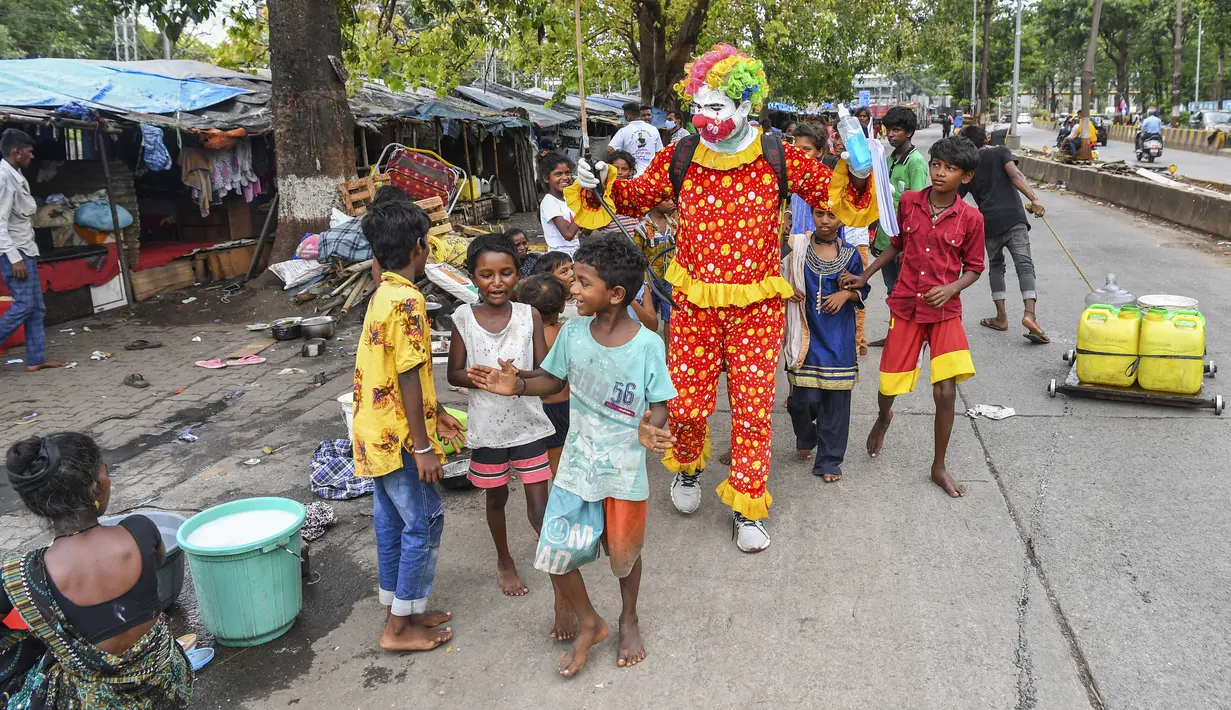 Relawan pekerja sosial, Ashok Kurmi berinteraksi dengan anak-anak saat mendisinfeksi ruang publik di daerah kumuh Mumbai pada 2 Juni 2021. Kurmi turun tangan memerangi virus Corona COVID-19 di daerah kumuh Mumbai menggunakan aksesori yang tidak biasa, yaitu kostum badut. (INDRANIL MUKHERJEE/AFP)