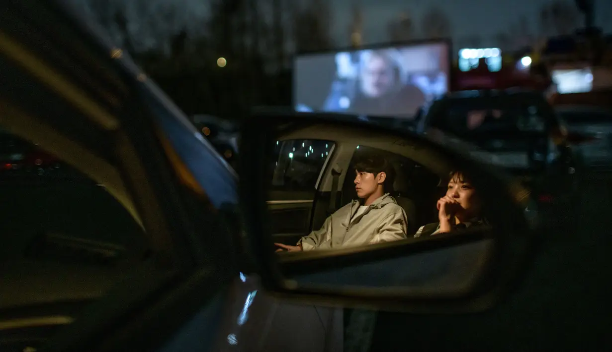 Sepasang suami istri duduk di mobil mereka ketika menonton pemutaran film di sebuah bioskop kendara atau drive-in cinema di Seoul, Korea Selatan, 21 Maret 2020. Jenis bioskop ini menjadi pilihan yang lebih bagi warga Seoul untuk menikmati film di tengah pandemi virus corona Covid-19. (Ed JONES/AFP)