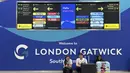 Para penumpang duduk di depan papan informasi yang menunjukkan lokasi meja maskapai di Bandara Gatwick dekat London, Inggris, Kamis 12 Juni 2025. (AP/Kin Cheung)