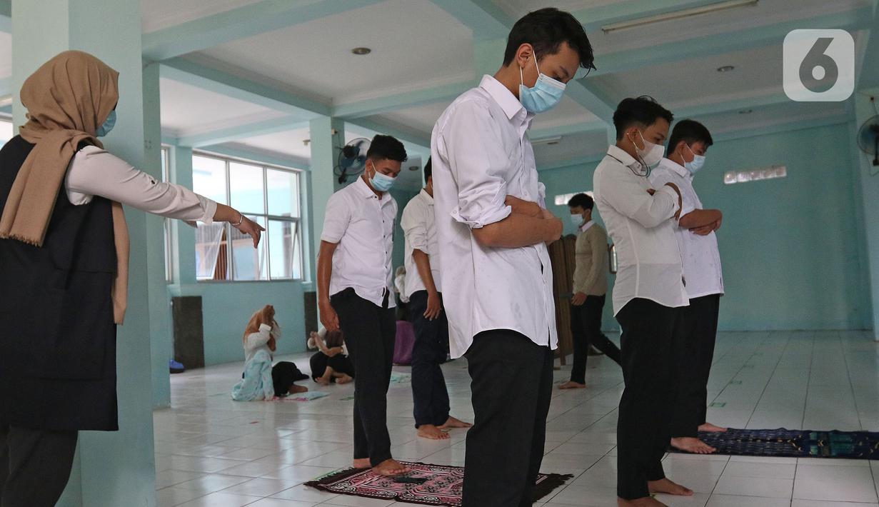 Guru yang juga satgas Covid-19 sedang melakukan pengawasan saat ibadah di SMKN 51, Jakarta, Rabu (7/4/2021). SMKN 51 melakukan uji coba masuk sekolah dan Uji Sertifikasi Kompetensi (USK) dengan protokol kesehatan yang ketat. (Liputan6.com/Herman Zakharia)